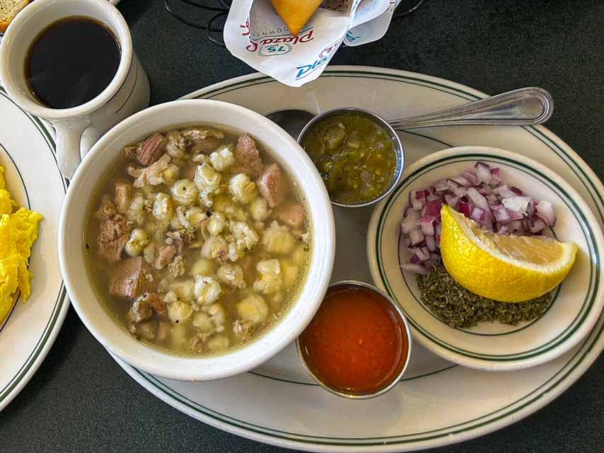 a bowl of white posole in Santa Fe New Mexico with accompanying red and green chile sauces